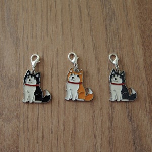 May include: Three metal charms featuring cartoon husky dogs in black, white, and orange. Each charm has a silver loop for attaching to a keychain or bag.