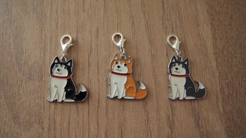 May include: Three silver charm pendants featuring cartoon husky dogs. The dogs are sitting and have different colored fur: black and white, orange and white, and black and white. Each charm has a silver loop for attaching to a chain or bracelet.