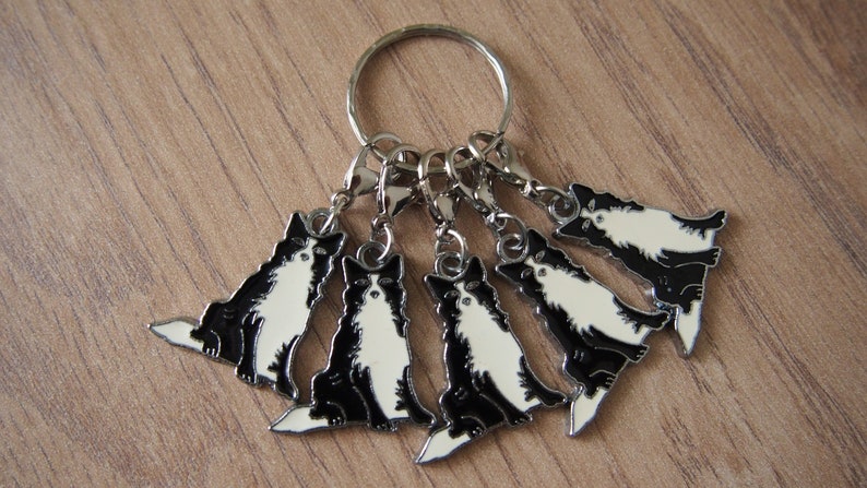 May include: A set of six black and white dog charm keychains with silver rings and clips. The charms are of a sitting dog breed with a white chest and white paws.