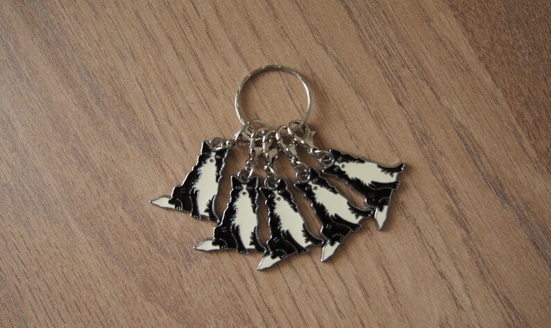 May include: A silver keychain with six black and white cat charms. The charms are attached to a silver ring.