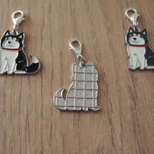 May include: Three metal charms featuring a black and white husky dog. One charm has a solid silver back, while the other two charms have a black and white husky dog design on the back.
