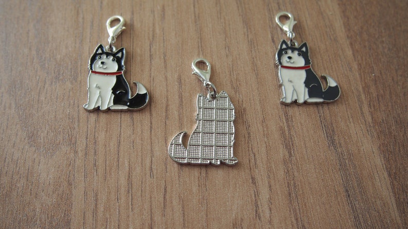 May include: Three metal charms featuring a black and white husky dog. One charm has a solid silver back, while the other two charms have a black and white husky dog design on the back.