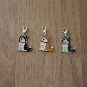 May include: Three metal charms featuring cartoon husky dogs in black, orange, and black and white. Each charm has a silver loop for attaching to a bag, keychain, or other item.