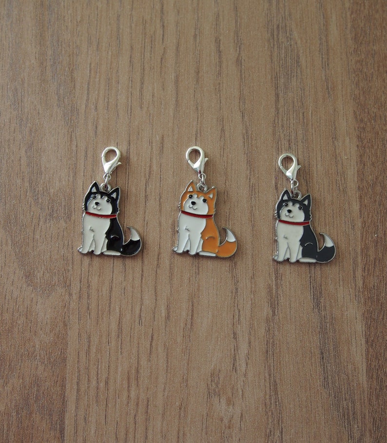 May include: Three metal charms featuring cartoon husky dogs in black, orange, and black and white. Each charm has a silver loop for attaching to a bag, keychain, or other item.