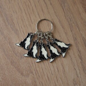 May include: A silver key chain with six black and white dog charms. Each charm features a different pose of a dog.