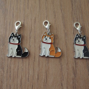 May include: Three metal charms featuring cartoon husky dogs in black, orange, and white. Each charm has a silver loop for attaching to a bag or keychain.