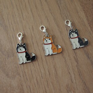 May include: Three silver charm pendants featuring cartoon husky dogs. The dogs are sitting and have different colored fur: black and white, orange and white, and black and white with a red collar.