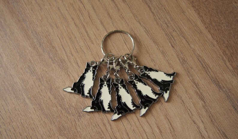 May include: A silver key chain with six black and white cat charms. The charms are attached to a silver ring and have a silver lobster clasp.