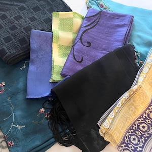 May include: Assortment of colorful scarves in various patterns and textures. Includes a dark blue scarf with a diamond pattern, a teal scarf with floral embroidery, and a black scarf with fringe.
