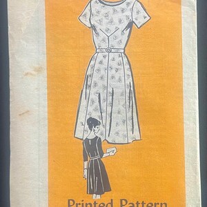 May include: Vintage printed sewing pattern featuring a dress illustration with a fitted bodice, short sleeves, and a flared skirt. The pattern includes a smaller illustration of a woman wearing a similar dress. The text "Printed Pattern" and size 18 1/2 are visible.