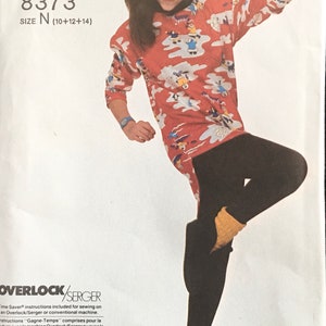 May include: A sewing pattern for a red and white patterned long-sleeved shirt and black leggings. The pattern is for sizes 10, 12, and 14. The pattern number is 8373. The pattern includes instructions for sewing on an overlock/serger or conventional machine.
