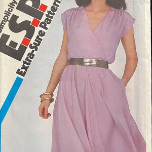 May include: A vintage Simplicity ESP Extra-Sure Pattern sewing pattern. The pattern features a light purple wrap dress with a metallic belt. The pattern size is O (12, 14, & 16).