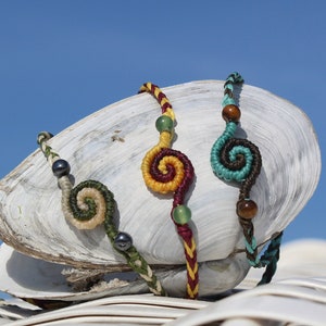 May include: Four colourful bracelets with spiral designs on a white seashell. The bracelets are made with different coloured threads and beads.