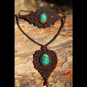 Op de afbeelding: Een bruine macramé ketting en armband set met een turquoise en bruine stenen hanger en een bijpassende armband. De set is versierd met kleine rode kralen.