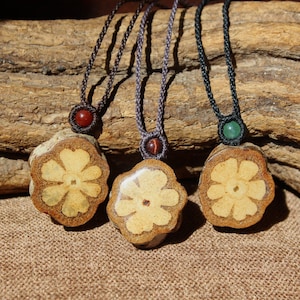 Può includere: Tre collane con ciondoli a forma di fiore in legno. I ciondoli sono di colore marrone chiaro con un contorno marrone più scuro. Ogni collana ha una perla di colore diverso: rosso, occhio di tigre e verde.