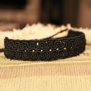 May include: A black braided bracelet with a detailed woven pattern.
