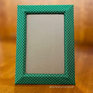 May include: A rectangular picture frame with a green fabric cover featuring a white polka dot pattern. The frame has a neutral gray interior and is displayed on a wooden surface. The text "@notesbytatianah" is visible at the bottom.