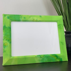 May include: A rectangular picture frame featuring a vibrant lime green finish with a mottled, watercolor-style texture. The frame has a wide, beveled border surrounding a blank, white rectangular center space, designed for displaying photographs or art.