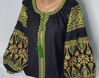 May include: Black embroidered blouse with green and gold floral patterns. The blouse has long sleeves and a round neckline.