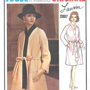 Könnte beinhalten: Ein Vintage-Schnittmuster für einen Mantel, das ein Model zeigt, das einen cremefarbenen Mantel mit einer schwarzen Schärpe und einem schwarzen Hut trägt. Das Schnittmuster stammt von Vogue Paris Original, entworfen von Lanvin, und datiert aus dem Jahr 2007.