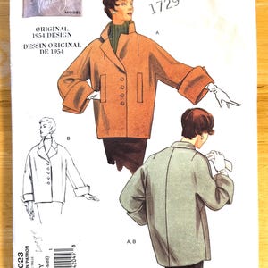 May include: Vogue Vintage Model sewing pattern V1023, an original 1954 design. The illustration shows a woman in a brown coat with large cuffs and a green turtleneck. The pattern includes views A and B, with the text "Large" and "(Sml-Med)".