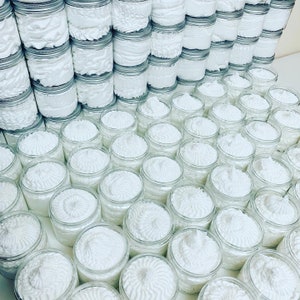May include: A large collection of white whipped body butter in glass jars. The jars are arranged in rows and columns, creating a visually appealing display.