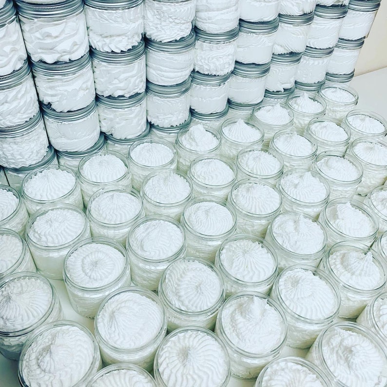 May include: A large collection of white whipped body butter in glass jars. The jars are arranged in rows and columns, creating a visually appealing display.