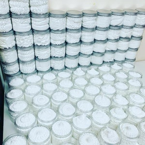 May include: A large collection of white whipped body butter in clear glass jars with silver lids. The jars are arranged in rows and columns, creating a visually appealing display.