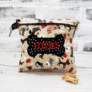 May include: A beige fabric treat pouch with a zipper closure and a black bone-shaped patch with white polka dots and the word "Treats" embroidered in red. The pouch is decorated with a pattern of cartoon dogs.