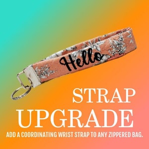 May include: A pink and white floral wrist strap with a silver key ring and the word "Hello" embroidered on it.  The strap is for adding to a zippered bag.