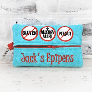 May include: A turquoise zippered pouch with red trim and a zipper pull. The pouch has three red circles with white borders and black text: "Gluten", "Allergy Alert", and "Peanut". The pouch also has red embroidered text that says "Jack's Epipens".