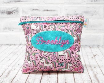 Könnte beinhalten: Rosa durchsichtige Tasche mit Reißverschluss und einem Einhorn-Druck und einem türkisfarbenen Oval mit dem Namen "Brooklyn" bestickt.