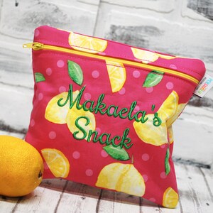 May include: Pink zippered pouch with a lemon print and white polka dots. The pouch has the text "Makaela's Snack" embroidered in green on the front.