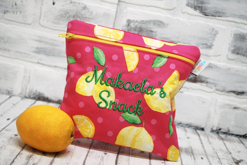 May include: Pink zippered pouch with a lemon print and white polka dots. The pouch has the text "Makaela's Snack" embroidered in green on the front.