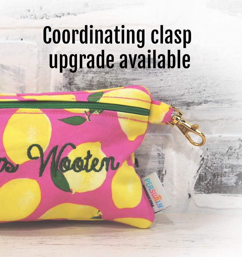 May include: Pink zippered pouch with a lemon print and the text "Wooten" embroidered on the front. The pouch has a gold metal clasp and a green zipper. The pouch is made by "PERSONally" and has a coordinating clasp upgrade available.