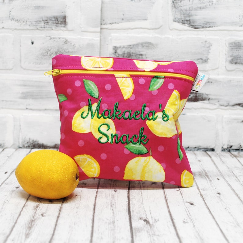 May include: Pink fabric zippered pouch with a lemon print and the text "Makaela's Snack" embroidered in green.