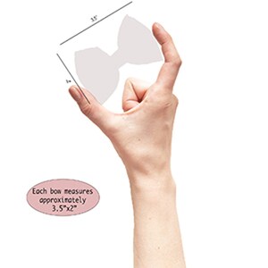 Puede incluir: Un lazo de color claro sostenido por una mano, con medidas de 8,9 cm x 5,1 cm. El lazo tiene una forma simple y sim&eacute;trica. El texto de la imagen dice: "Each bow measures approximately 3.5"x2"."