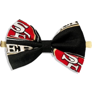 May include: A black and red bow tie with a white and gold design. The bow tie has a black center and a tan clip. The bow tie is a fan accessory.