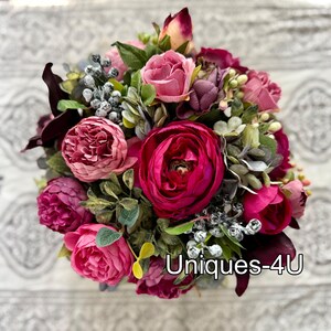 May include: A vibrant bouquet of artificial flowers in shades of pink, fuchsia, and burgundy. The arrangement includes roses, peonies, and other greenery. The text "Uniques-4U" is visible on the bottom right.