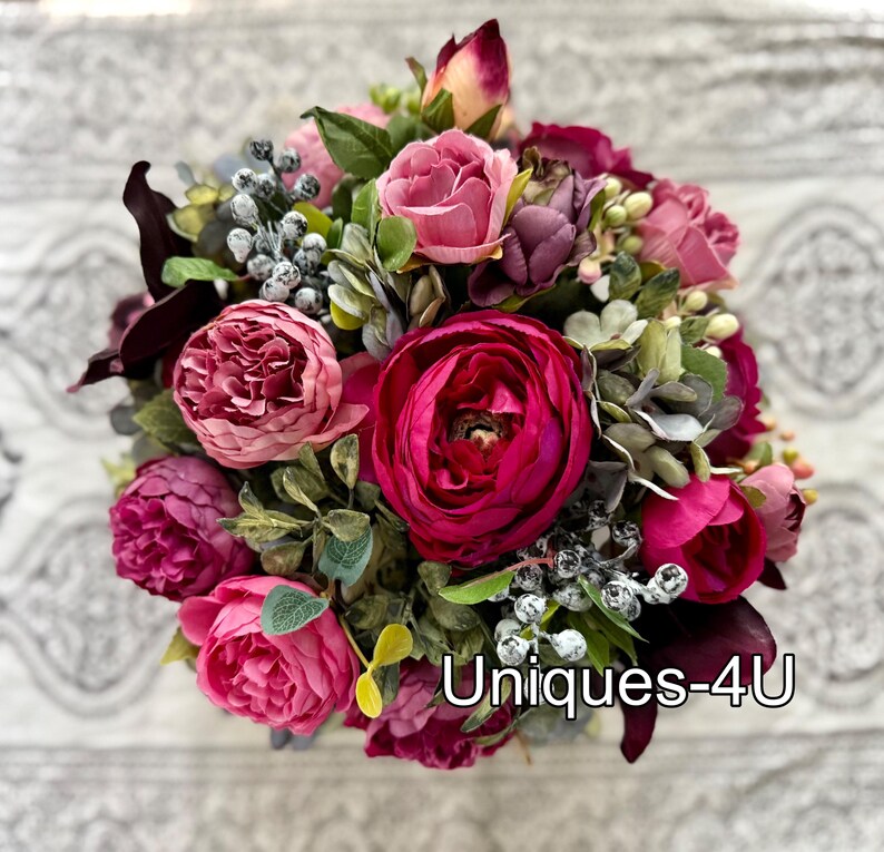 May include: A vibrant bouquet of artificial flowers in shades of pink, fuchsia, and burgundy. The arrangement includes roses, peonies, and other greenery. The text "Uniques-4U" is visible on the bottom right.
