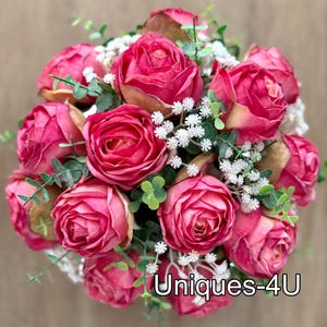May include: A bouquet of vibrant pink roses with touches of gold, white, and green foliage. The arrangement includes small white flowers and green leaves, with the text "Uniques-4U" at the bottom.