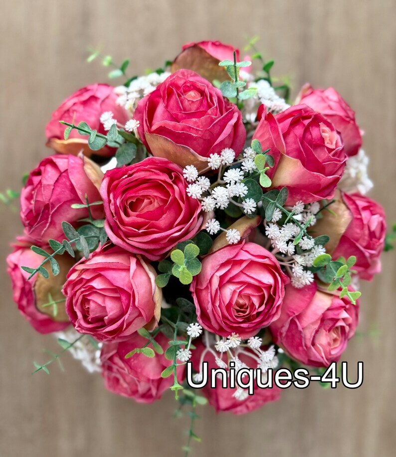 May include: A bouquet of vibrant pink roses with touches of gold, white, and green foliage. The arrangement includes small white flowers and green leaves, with the text "Uniques-4U" at the bottom.