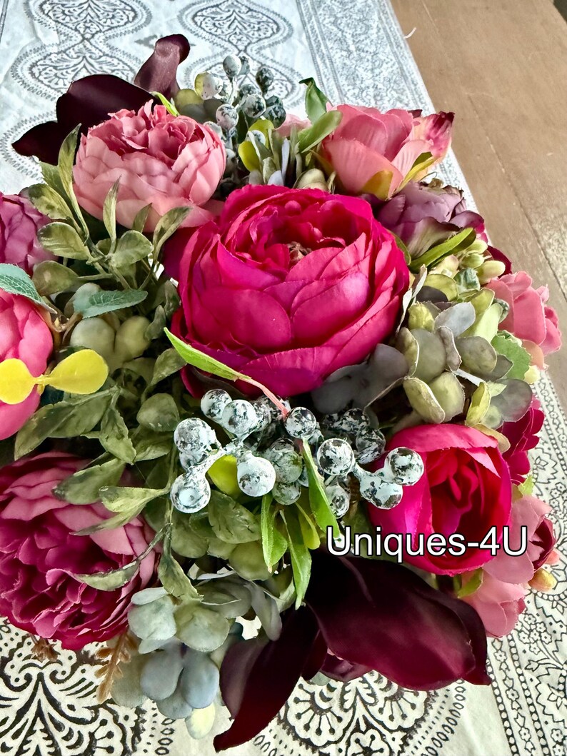 May include: A vibrant floral arrangement featuring large, deep pink peonies as the focal point, complemented by smaller pink and burgundy blooms. Green foliage and frosted berries add texture. The text "Uniques-4U" is visible.