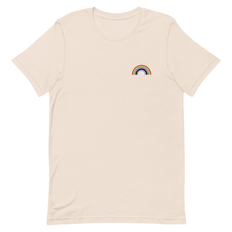 May include: A beige t-shirt with a small rainbow embroidered on the left chest.