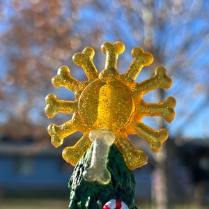 May include: A small, green, artificial Christmas tree decorated with a candy cane and a golden star-shaped ornament with a bone design. The star is made of plastic and has a glittery finish.