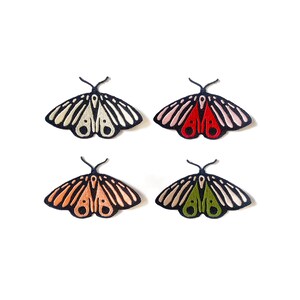 May include: Four embroidered moth patches in a variety of colors. Each moth has a black outline with detailed wing patterns. The colors include white, red, orange, and green, all set against a white background.