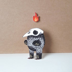 May include: A black and white creature with a skull head and a flame on top. The creature has a beak and is standing on a white surface.