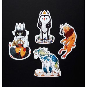May include: Four colorful stickers featuring whimsical animal characters. A black cat with a crown plays a trumpet, a white bird with a crown stands on a branch, a white and blue creature with a crown stands on a brown surface, and a brown and orange creature with a crown stands on a white surface.