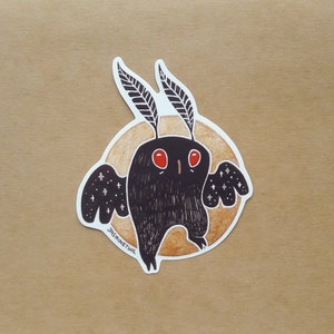 May include: A black and white sticker of a moth with red eyes and a starry pattern on its wings. The moth is on a brown and orange background with the text "JASMINETWIL" at the bottom.