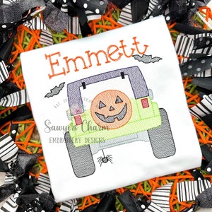 May include: White embroidered t-shirt with the name "Emmett" and a green Jeep with a jack-o-lantern in the back. The Jeep has bats flying above it and a spider hanging from the back bumper.